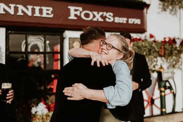 Guest warmly embracing the groom outside Johnnie Fox’s Pub during a wedding celebration.