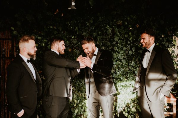 Groomsmen laughing and celebrating outdoors against ivy backdrop at Johnnie Fox’s