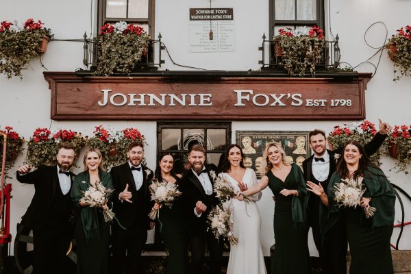 Wedding party celebrating outside Johnnie Fox’s pub with bouquets and formal wear