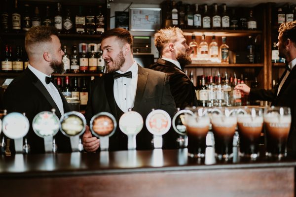 Groomsmen in tuxedos chatting at the bar with Guinness taps in front at Johnnie Fox’s