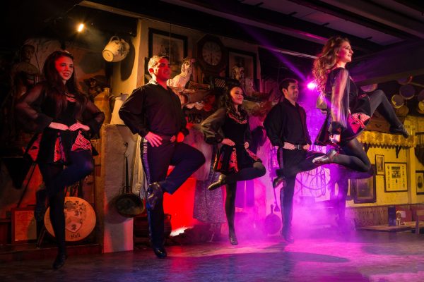 Irish dance performers mid-routine on the Hooley stage with colourful lighting