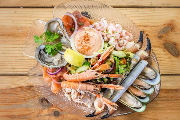 Mixed seafood platter with prawns, oysters, mussels, smoked salmon, salad, and lemon on a glass plate