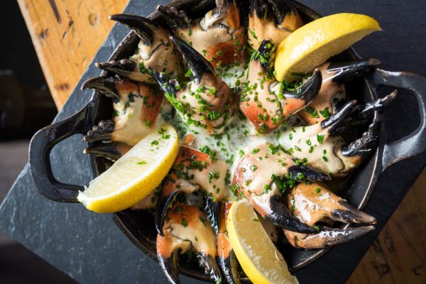 Crab claws in garlic butter with lemon wedges served in a cast-iron dish
