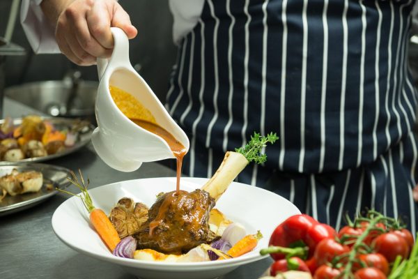 Chef plating roasted meat with vegetables beside fresh produce in the kitchen at Johnnie Fox’s