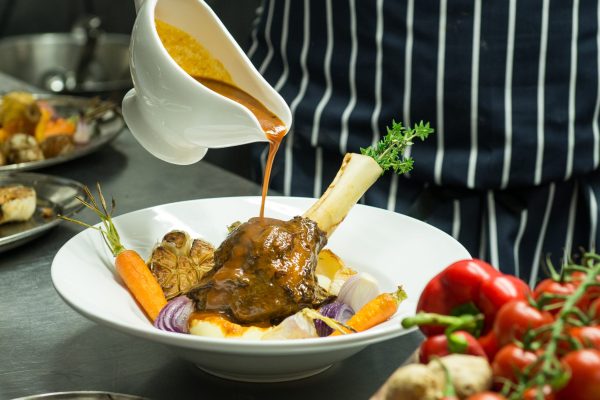 Chef pouring sauce over plated lamb shank with vegetables in the kitchen at Johnnie Fox’s
