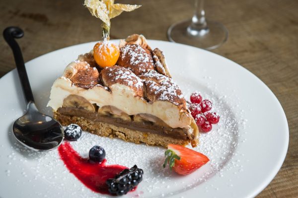 Slice of berry tart with powdered sugar, fresh berries, and sauce on a white plate