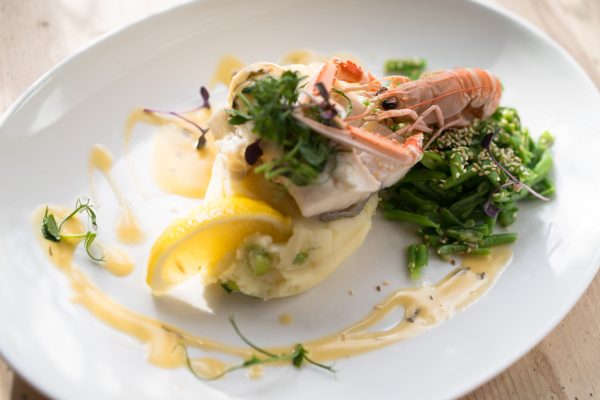 Fillet of fish with prawns, mashed potato, greens, and lemon on a white plate