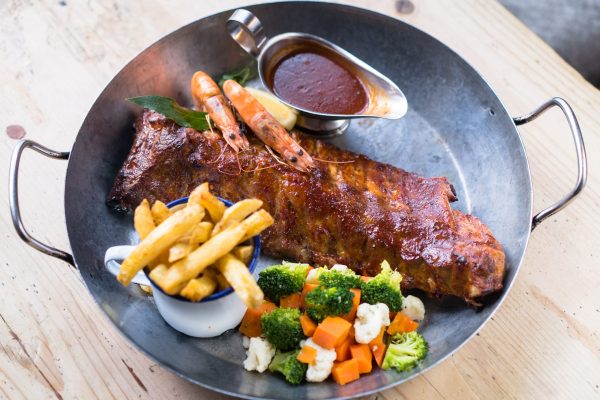 Barbecue ribs with chips, sauce, and mixed vegetables on a metal platter