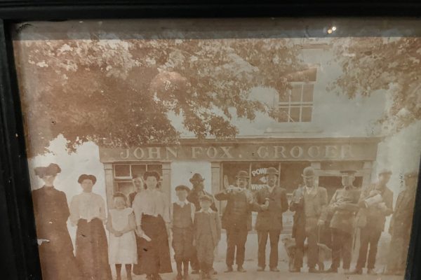 Historic group photo outside John Fox Grocer circa 1890, showing men, women and children in traditional dress.
