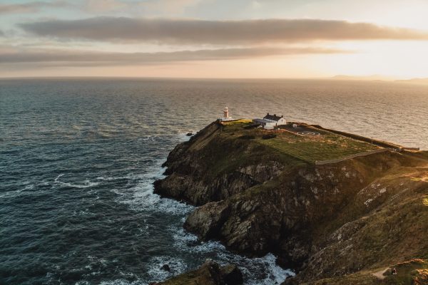 Aerial view of Howth lighthouse on a cliff at sunset with waves below