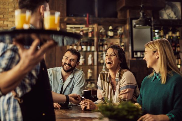 Cheerful friends having fun while talking to a waiter in a cafe.